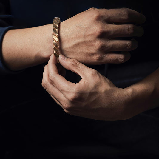 Close-up of a hand wearing a copper gold bracelet on a dark background
