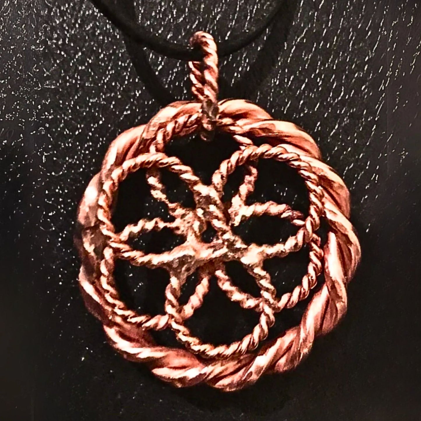 Copper-colored woven pendant on a black background