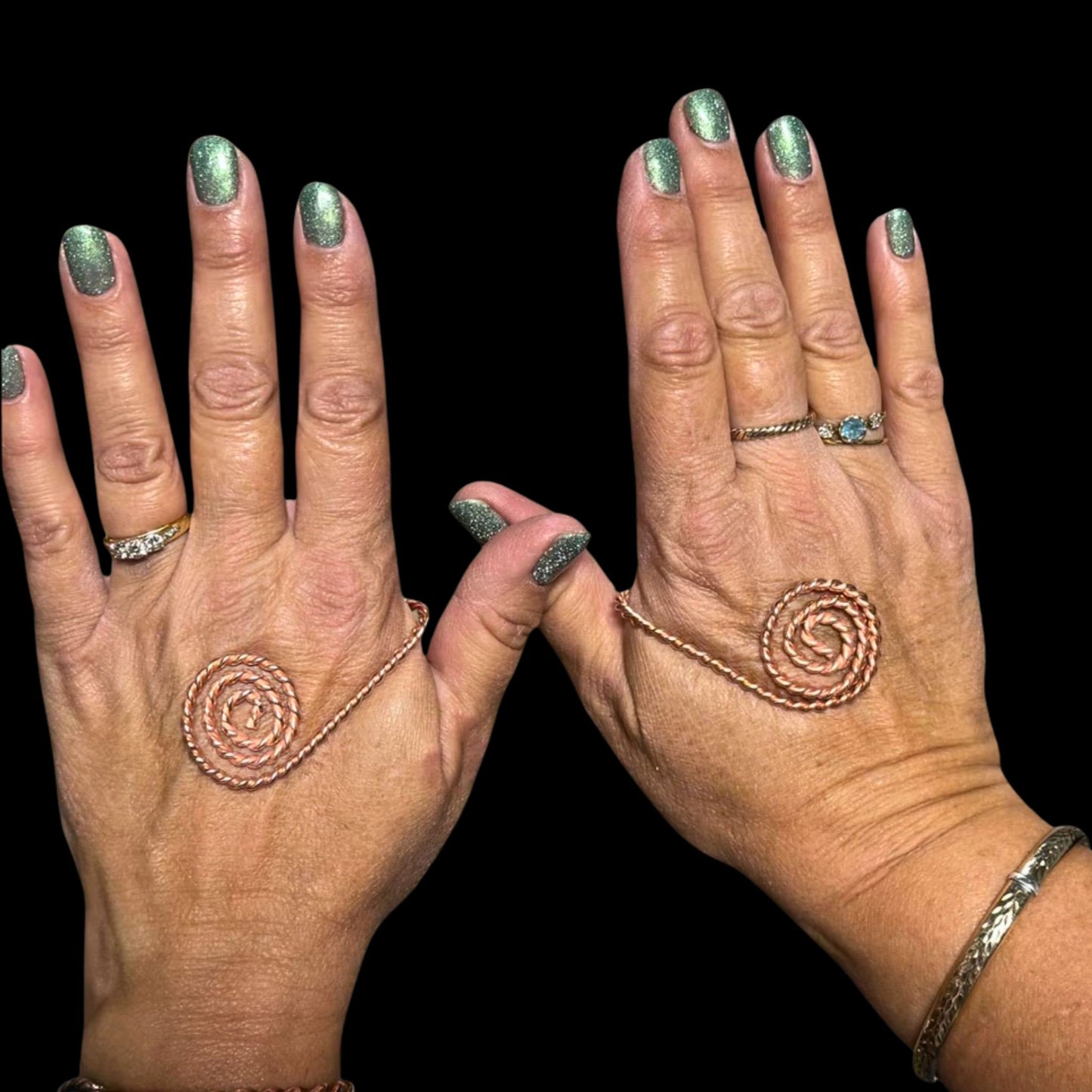 Two hands with spiral designs on fingers and palms against a black background
