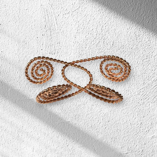 Decorative copper spiral EMF hand healing cuffs with swirling design on a textured white wall