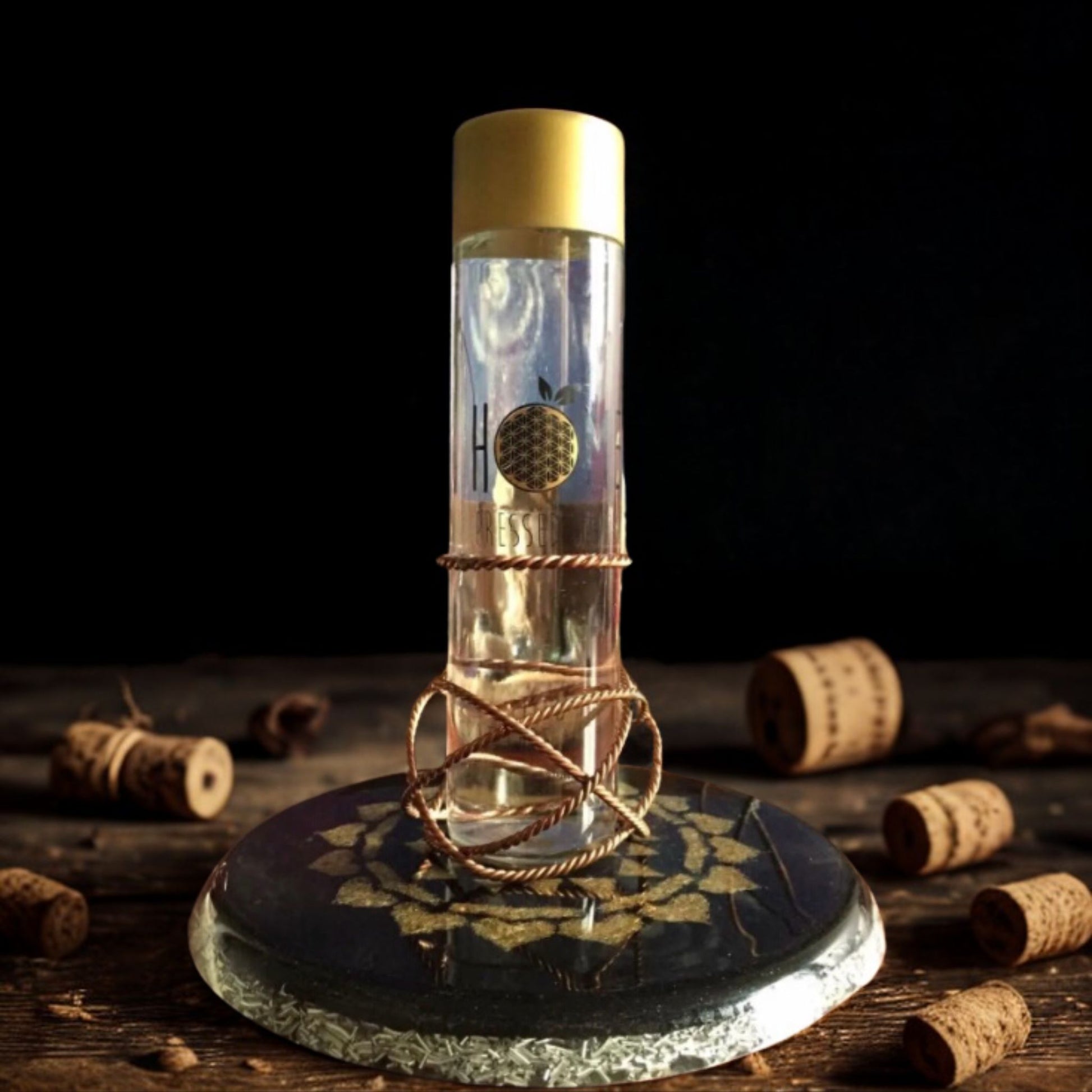 Clear bottle with gold cap on a dark stone base surrounded by corks