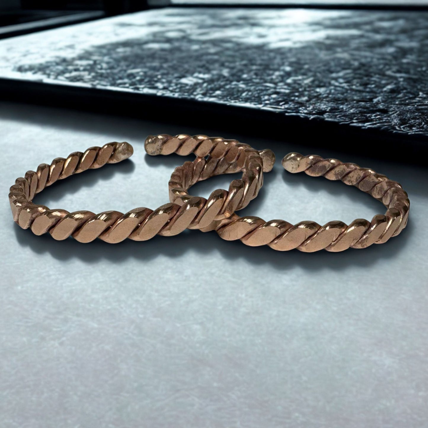Rose gold braided bracelet on a light gray surface with a dark background