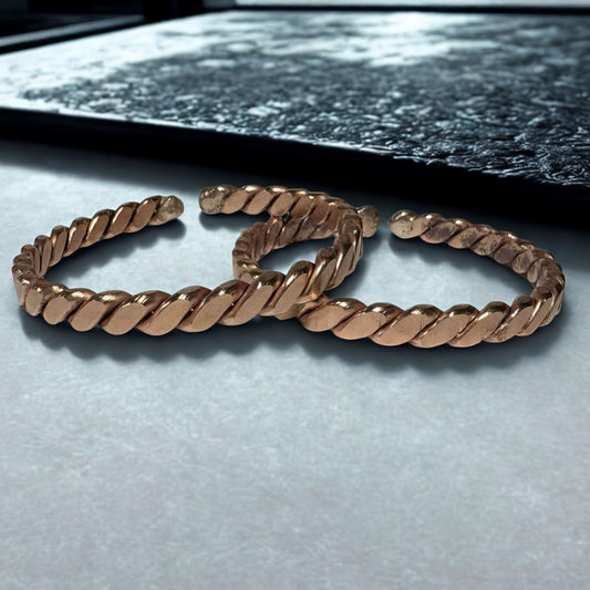 Rose gold braided bracelet on a light gray surface with a dark background