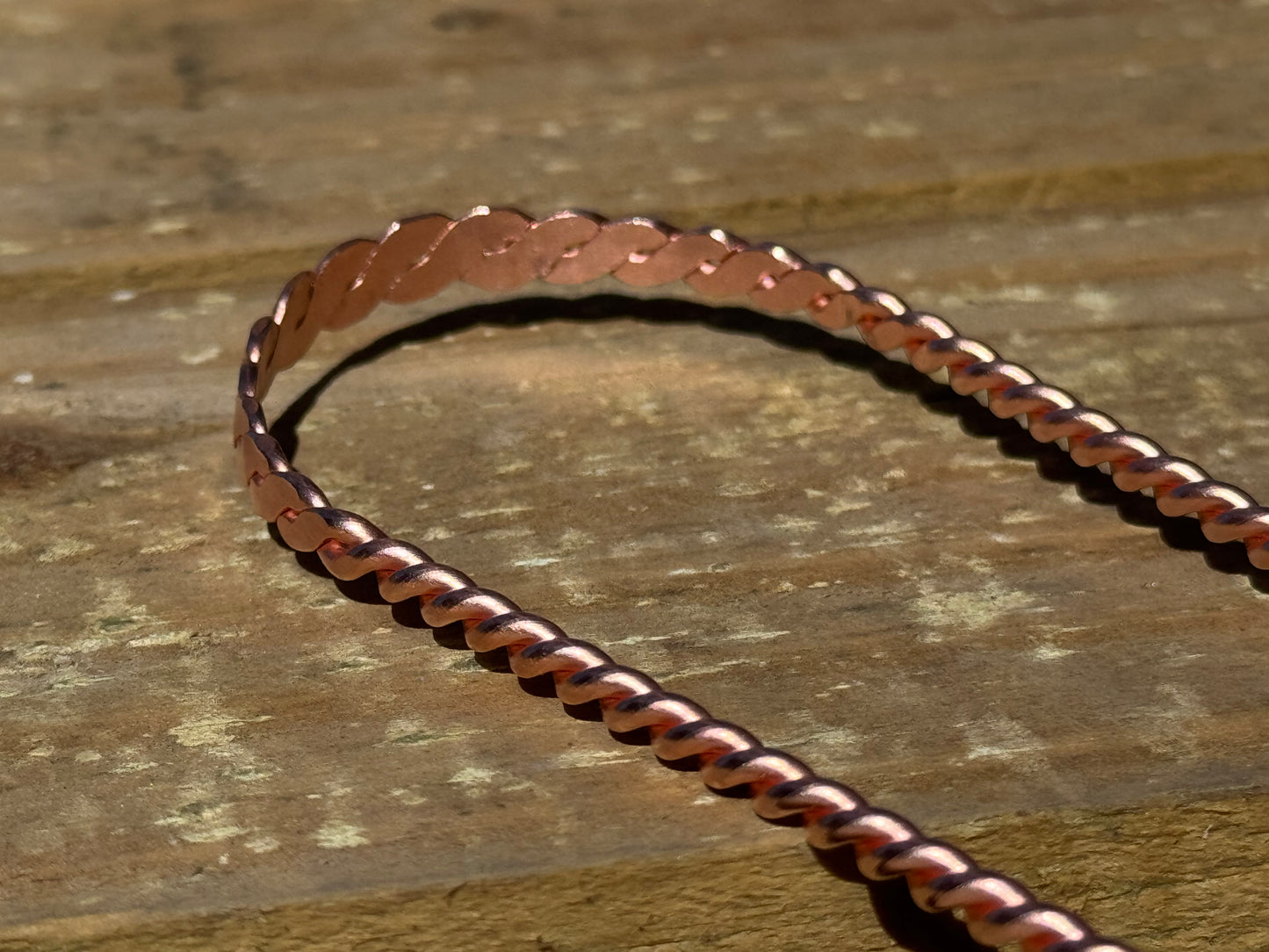 Copper tongue scraper chain on a wooden surface