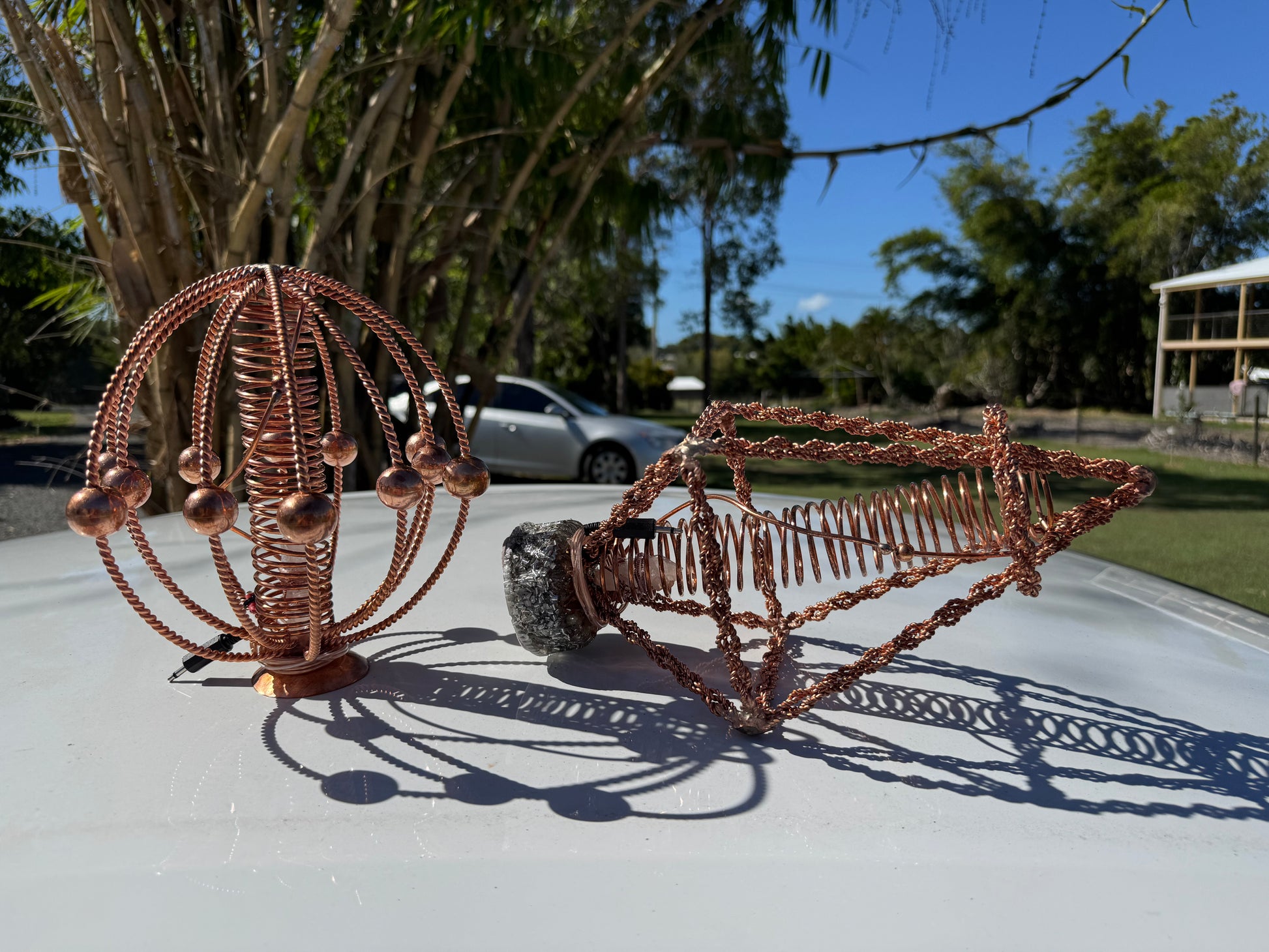 Copper wire sculptures on a car hood with trees and a building in the background