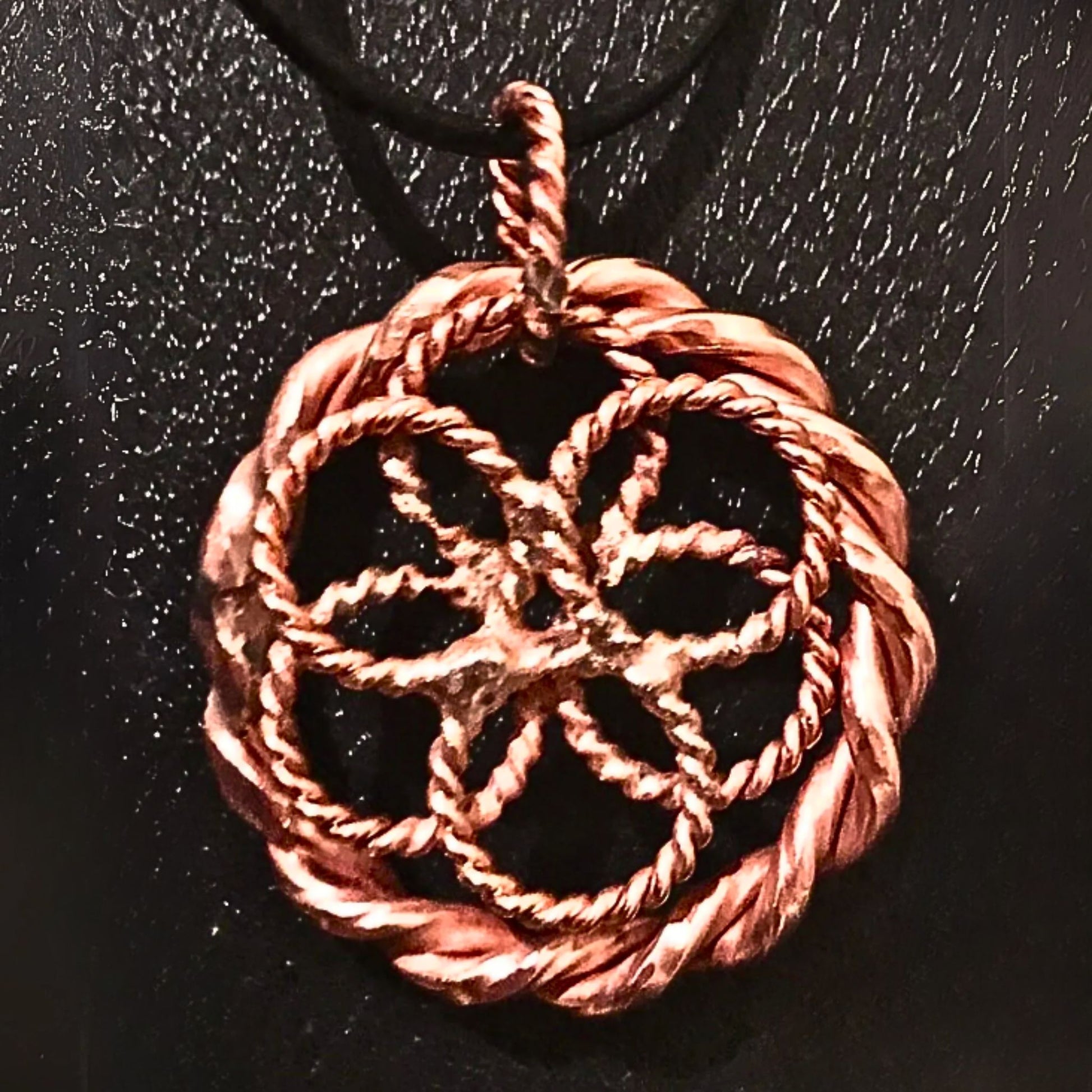 Copper-colored woven pendant on a black background
