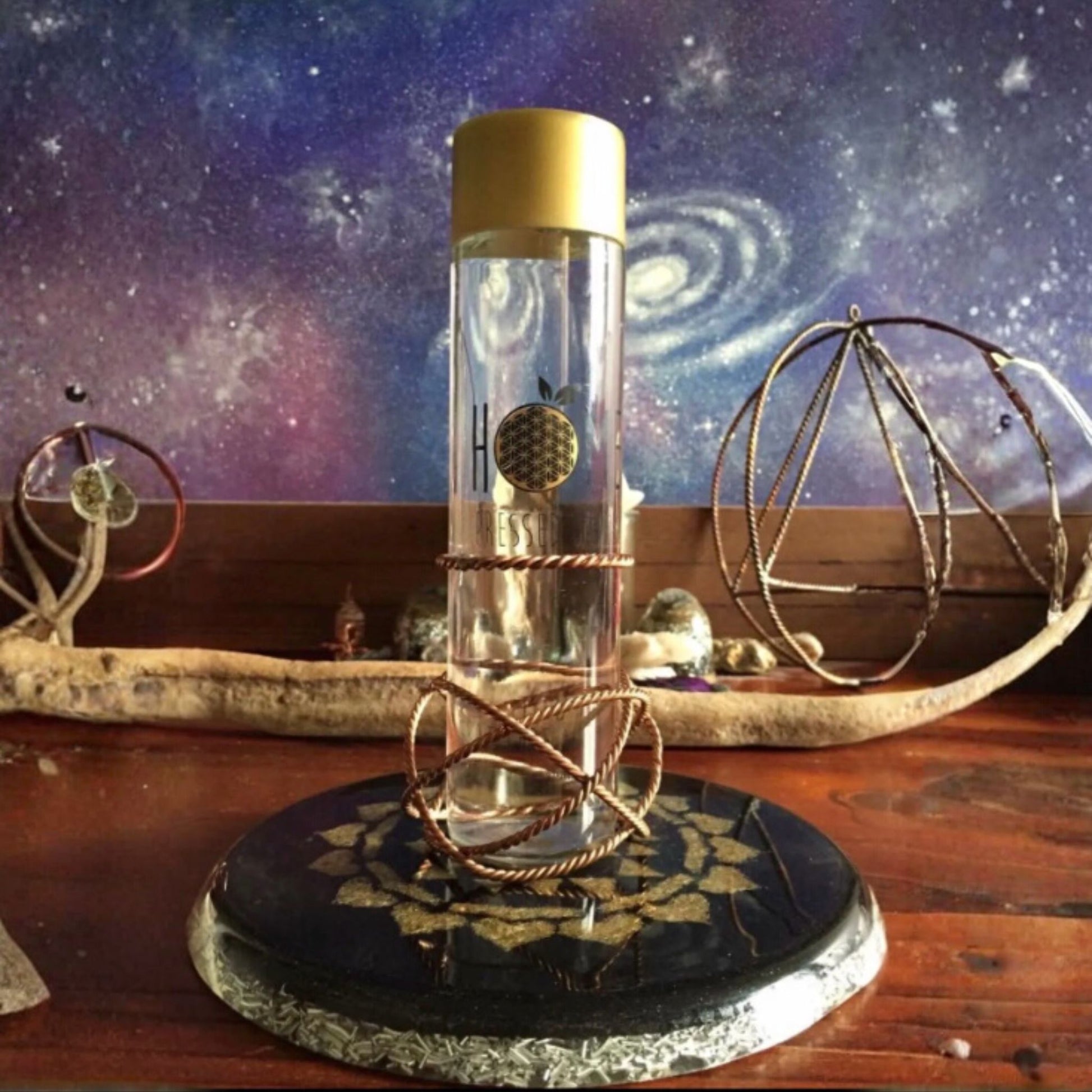 Clear bottle with gold cap on a decorative stand against a cosmic-themed background