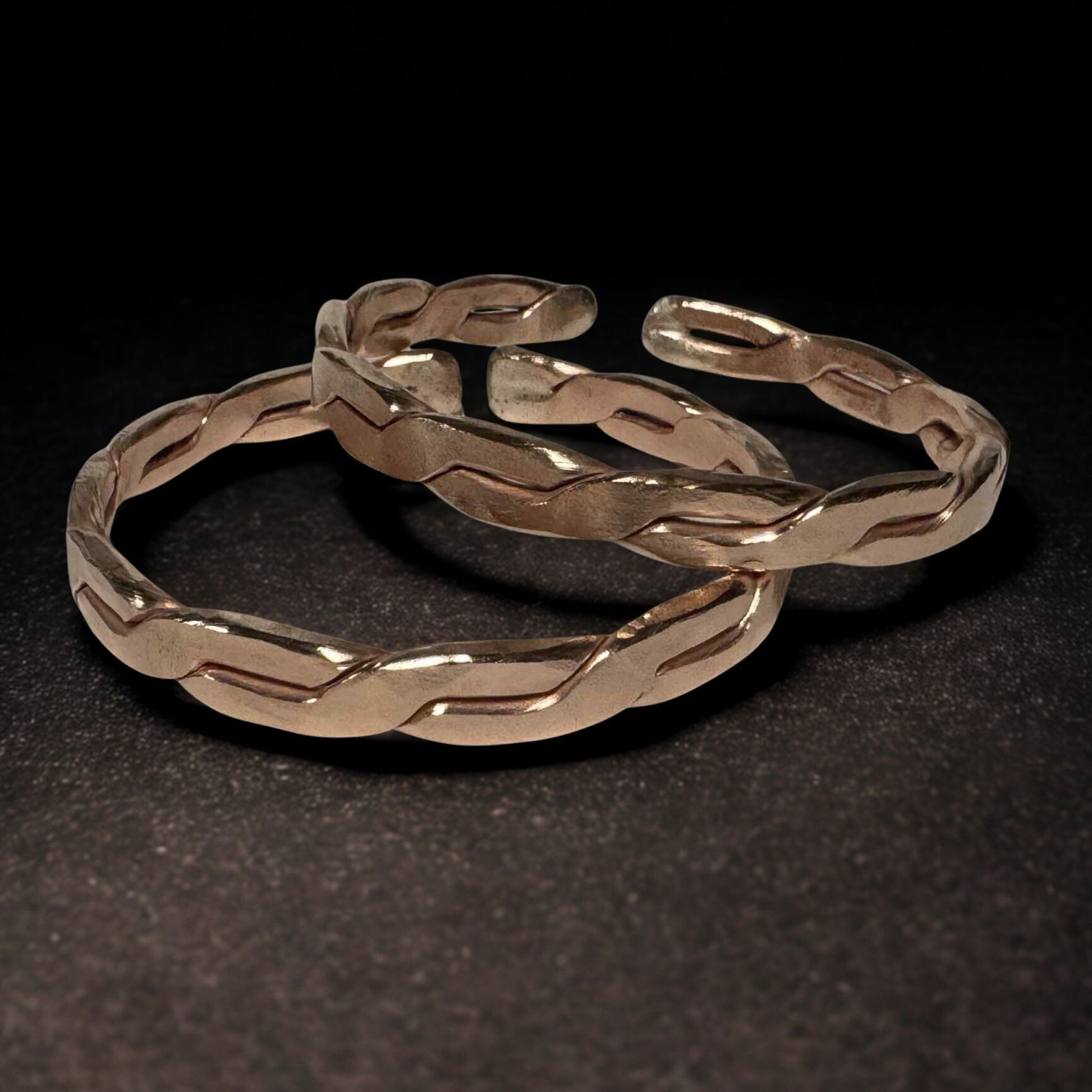 Two gold bracelets with braided design on a black background