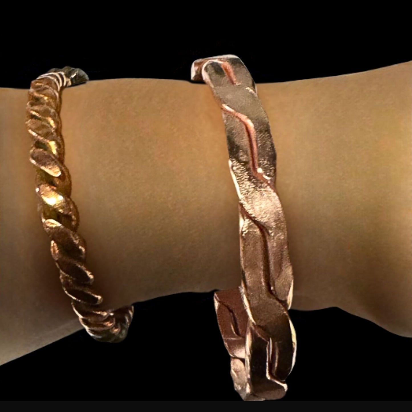 Two gold bracelets on a wrist against a black background