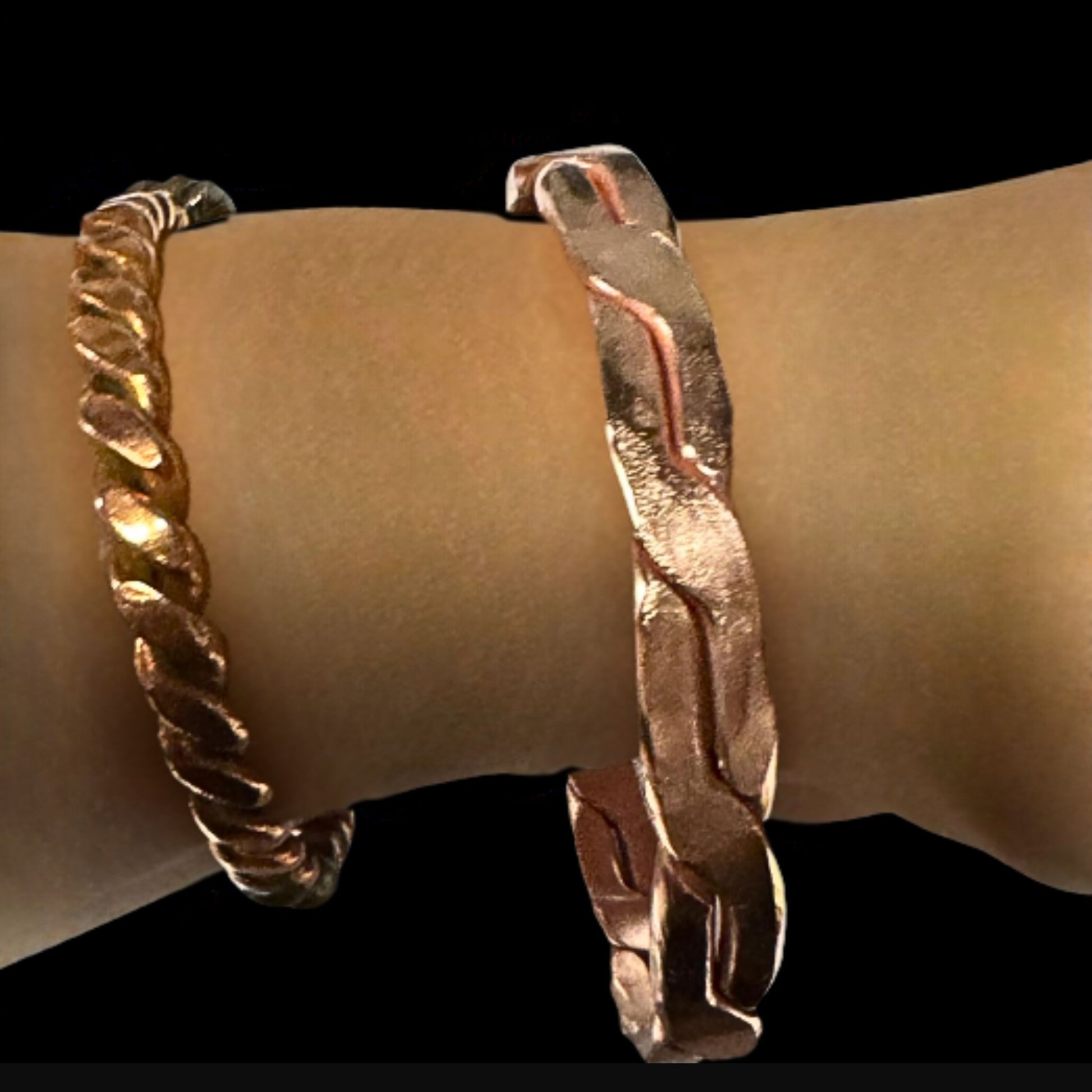 Two gold bracelets on a wrist against a black background